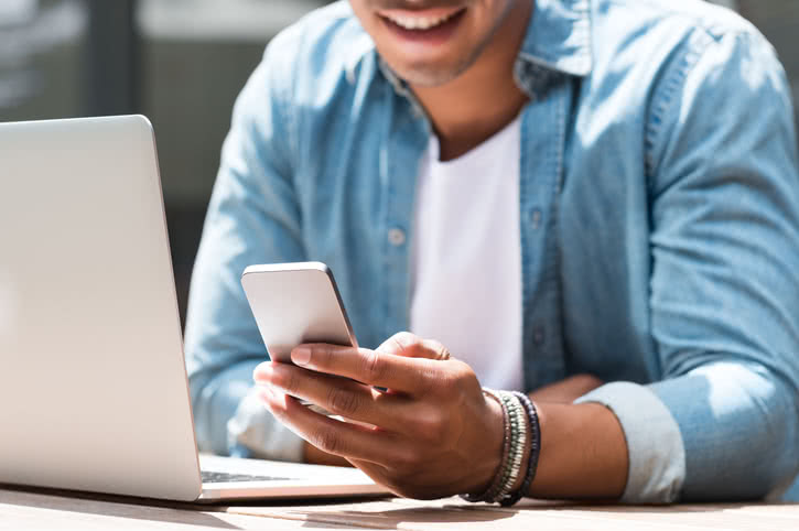 Smiling man takes a break from his laptop to look at his phone.