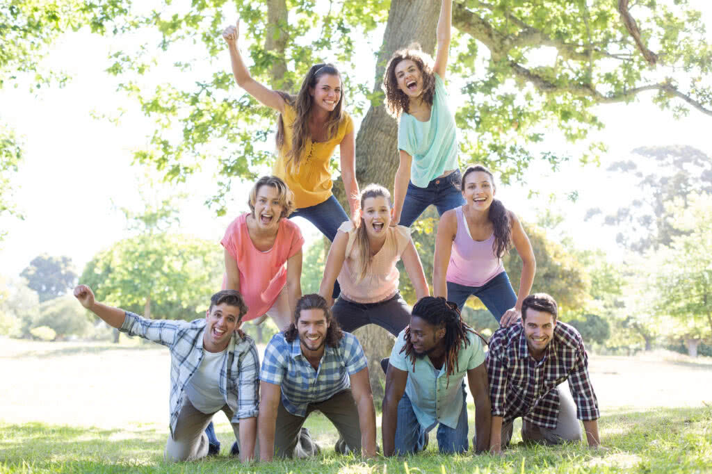 Group of happy people at a sunny park forming a human pyramid