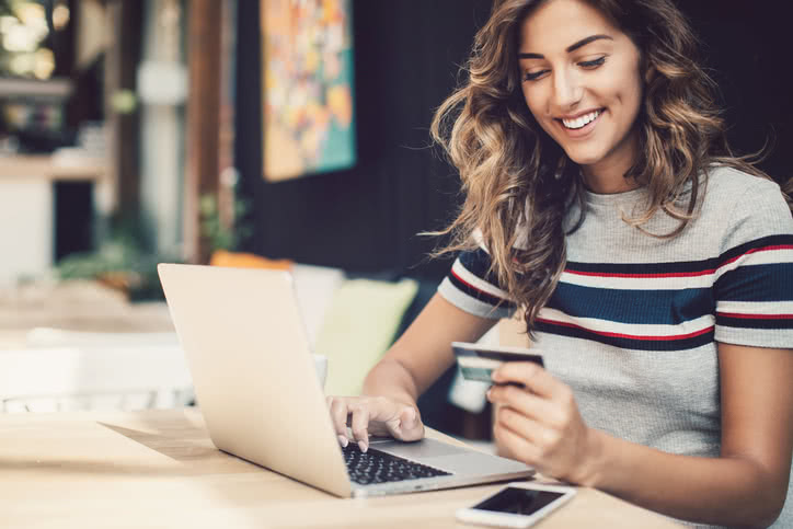 Smiling young woman holding a credit card and typing on a laptop.