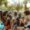 A group of men and women sit on the floor in a Vibes In The Park event drinking beer and laughing.
