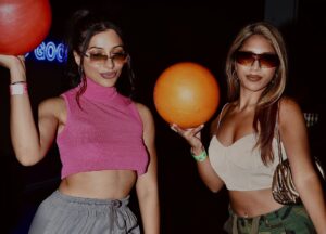 Two women hold bowling balls and pose for a photo at BennyBoys The Bowl event.