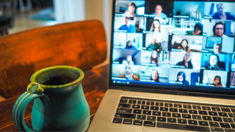POV of virtual conference attendee's desktop showing their coffee mug, the laptop screen, and all the other virtual conference attendees.